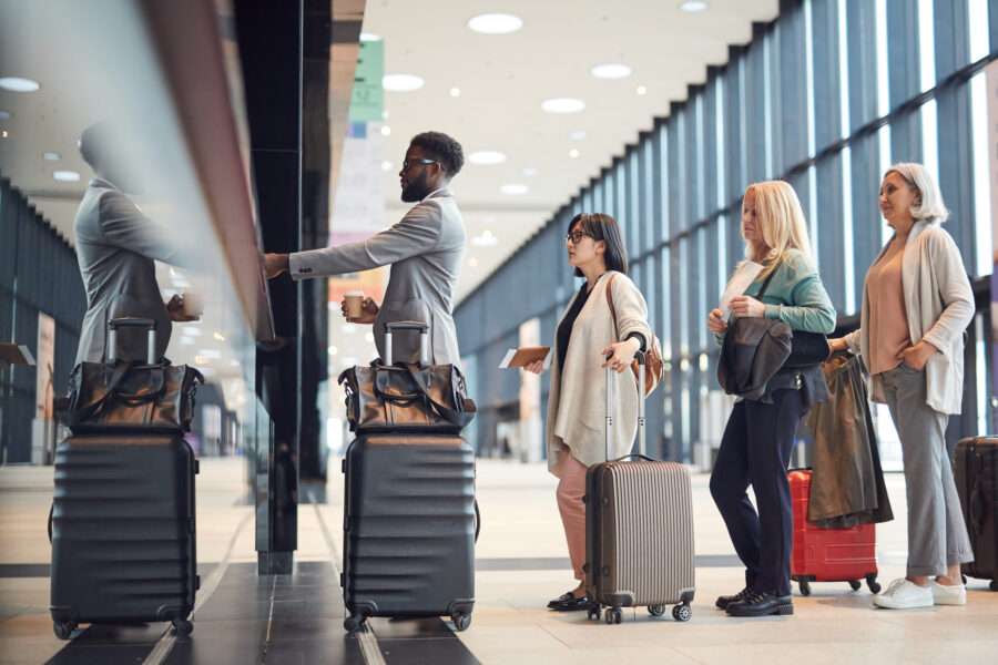 People standing in the queue with their carry-on luggage at the airport check-in counter.