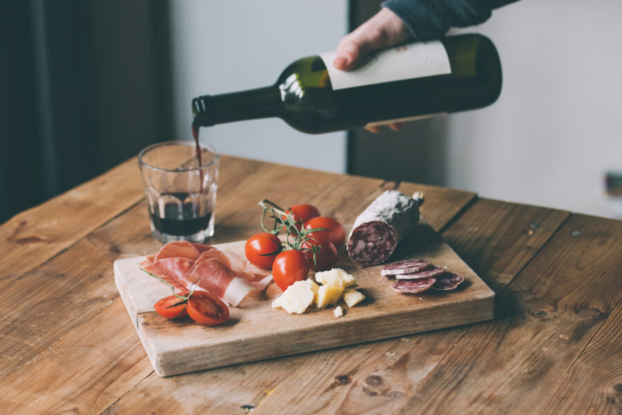 Spanish Appetizers - tomato, meat and cheese - on wooden board with bottle of wine and glass.