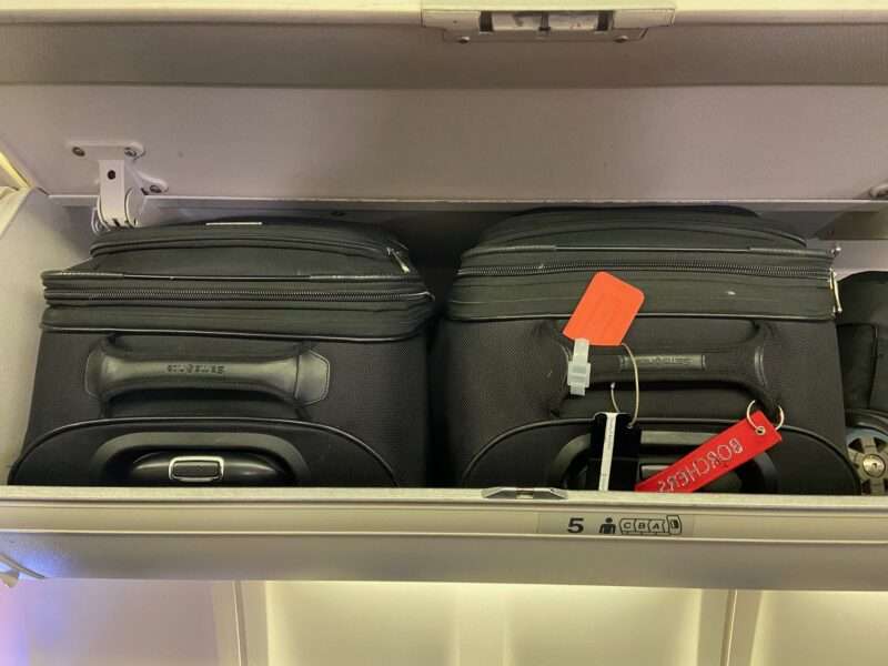 Carry-ons with name tags are in the above-seat storage bins.